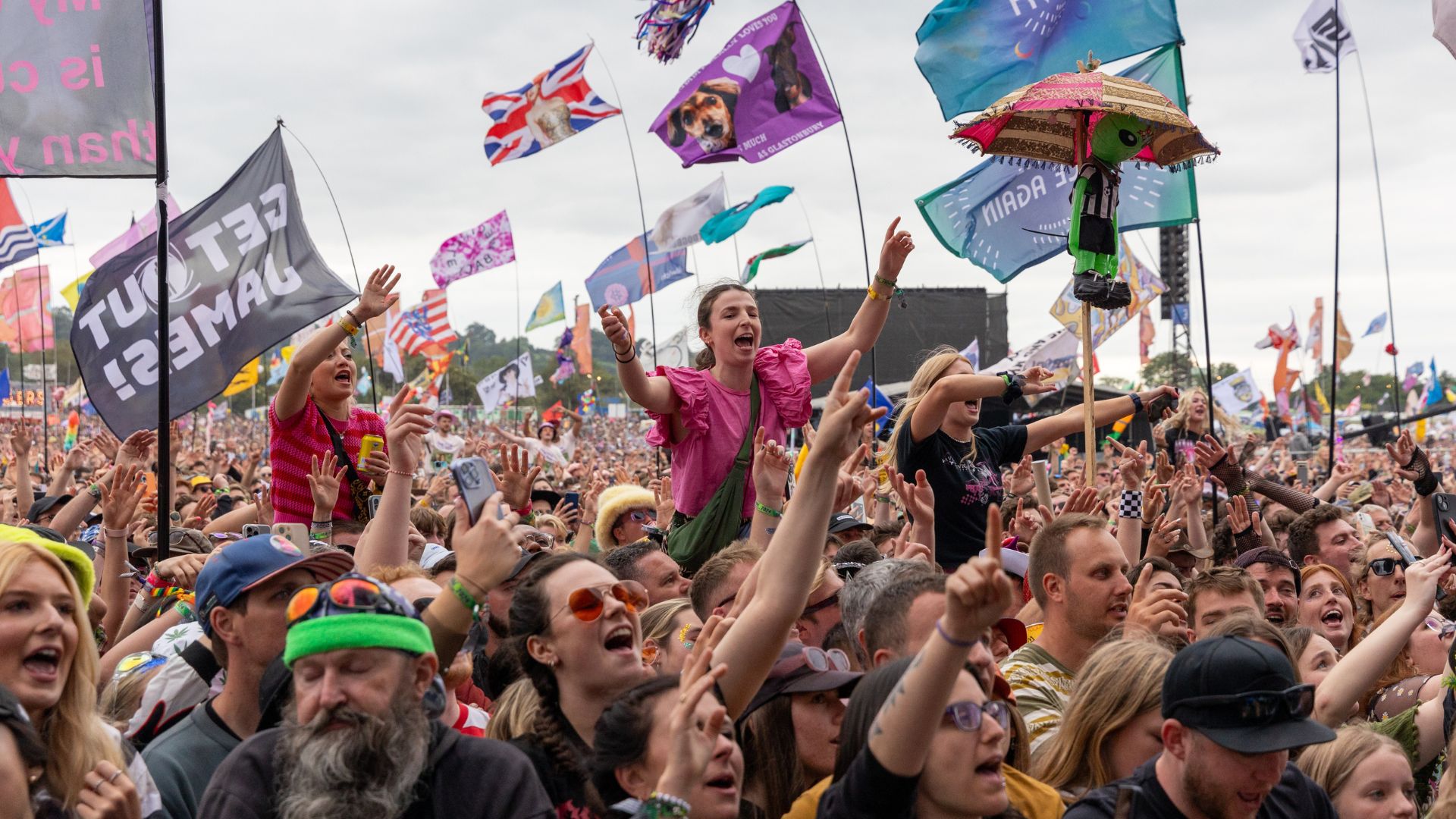 an image of a festival crowd at Glastonbury festival. There are people on other people's shoulders and lots of people waving flags