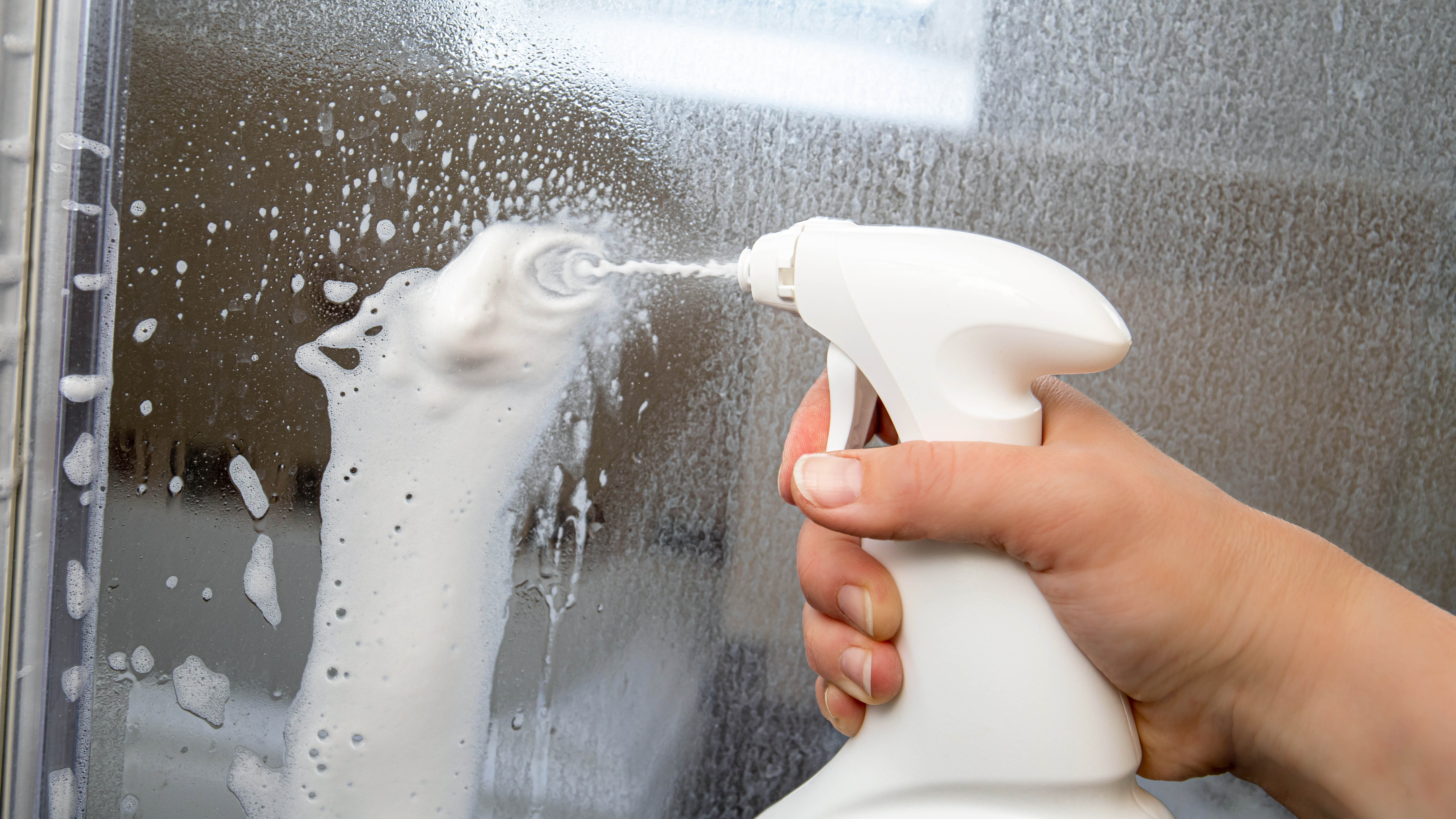 Someone cleaning limescale from a glass shower panel