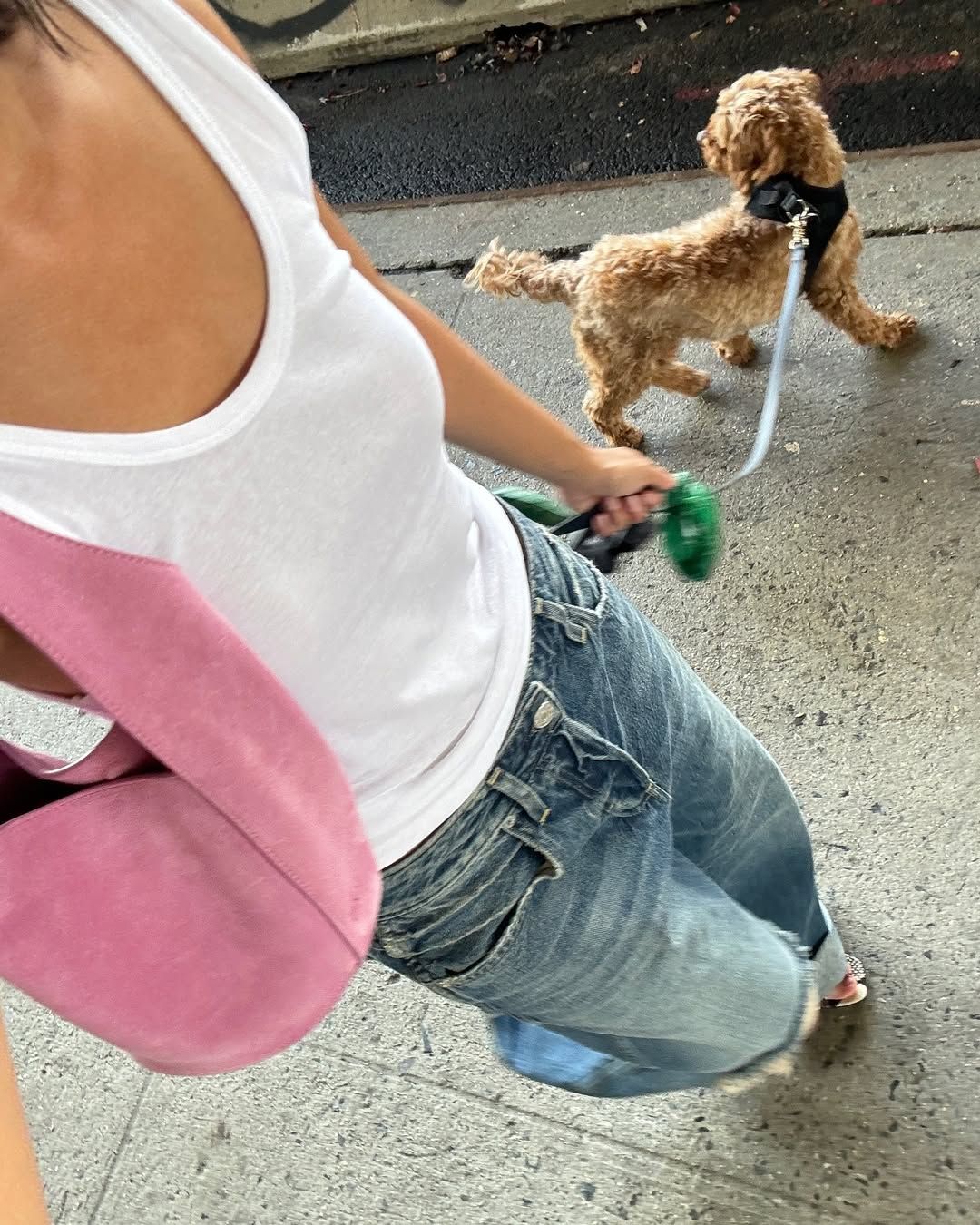 Woman wearing loose jeans with fitted white tank and pink purse in a summer 2025 outfit.