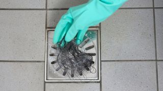 A gloved hand removing hair from a shower drain