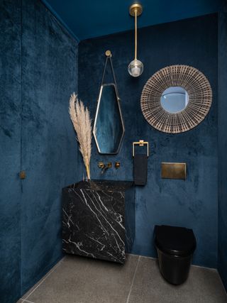 A blue velvet bathroom with marble sink, statement mirrors and hanging light fixture