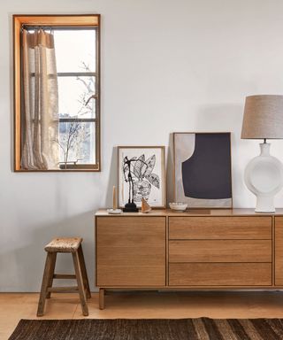 wood sideboard with slatted front and white sculptural table lamp and monochrome artworks