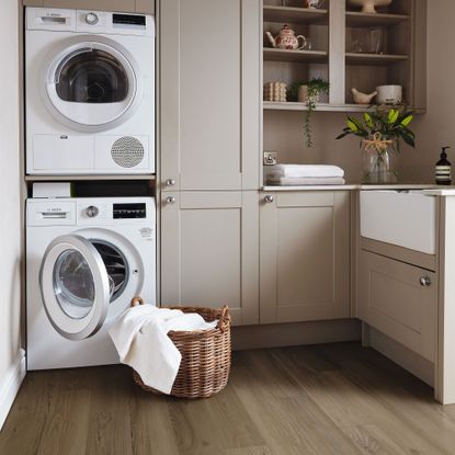 Utility room with wood LVT floors, taupe cabinetry and stacked washer dryers