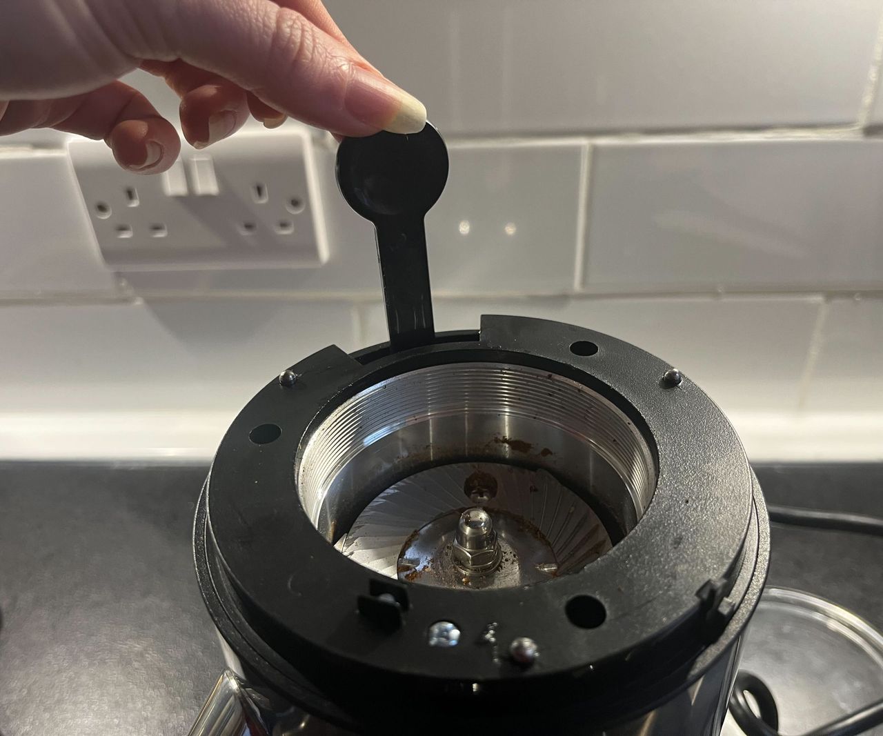 Fingers picking the Aarke Coffee Grinder cleaning brush from its compartment beside the burrs