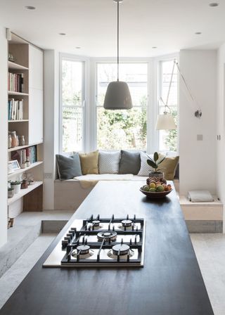 A kitchen extension that also has a book shelf as well as window seating. By the window is a bench with lots of cushions