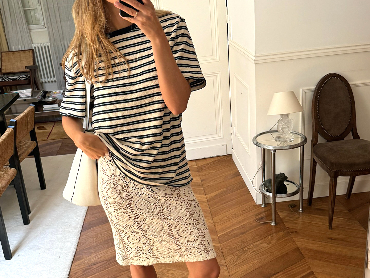 Influencer Anne Laure Mais wears a sheer lace skirt and an oversized striped crewneck top. She sports a white leather shoulder bag and MiuMiu ballet flats.