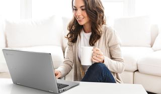 Woman uses Acer Chromebook in a living room while drinking coffee.
