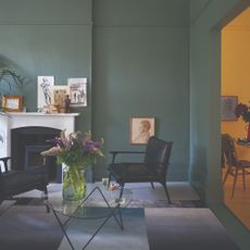 A green living room painted in Farrow & Ball's Green Smoke shade with a white fireplace and two black accent chairs