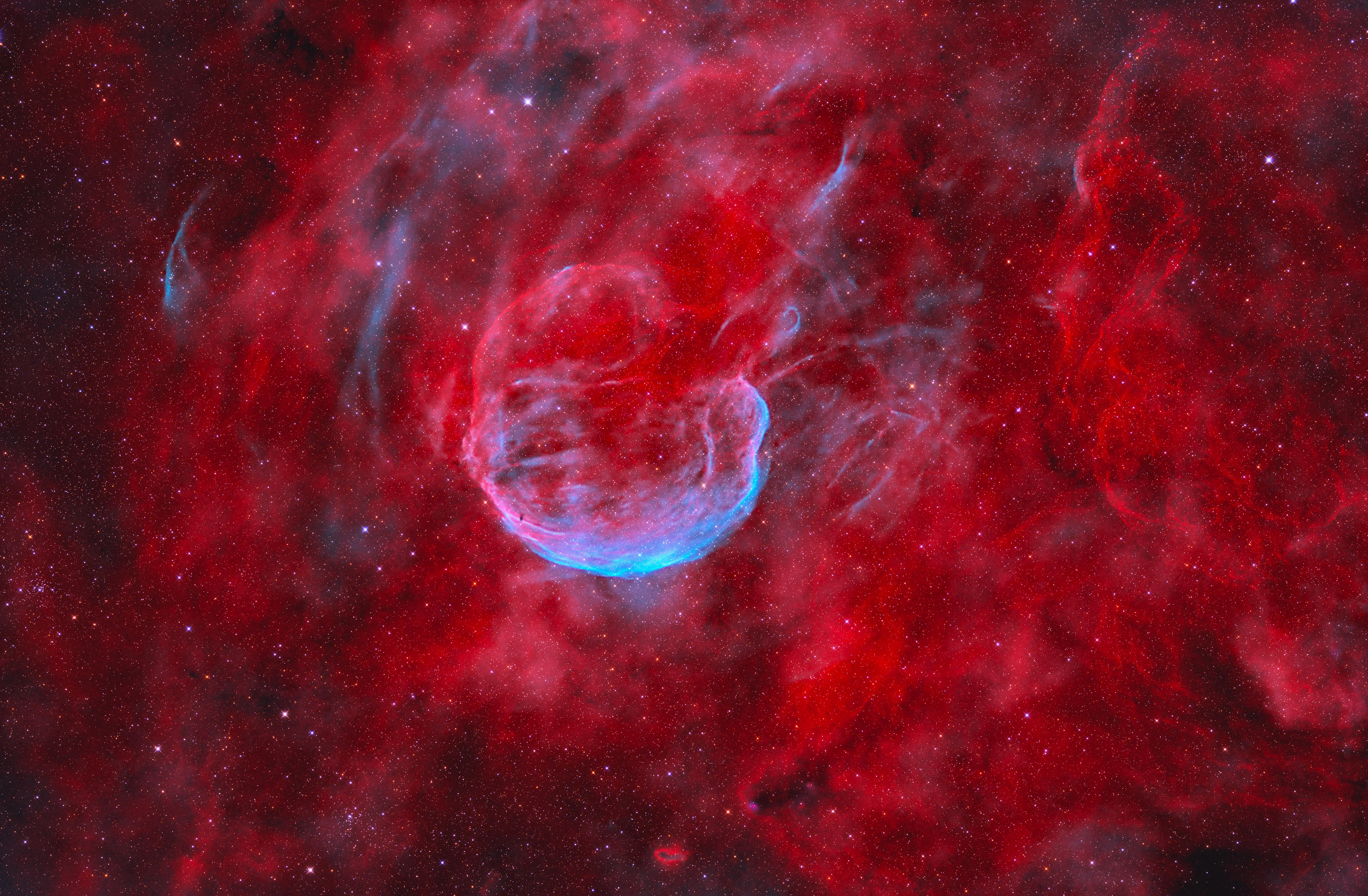 A cloud of blue gas glows amidst red dust in outer space