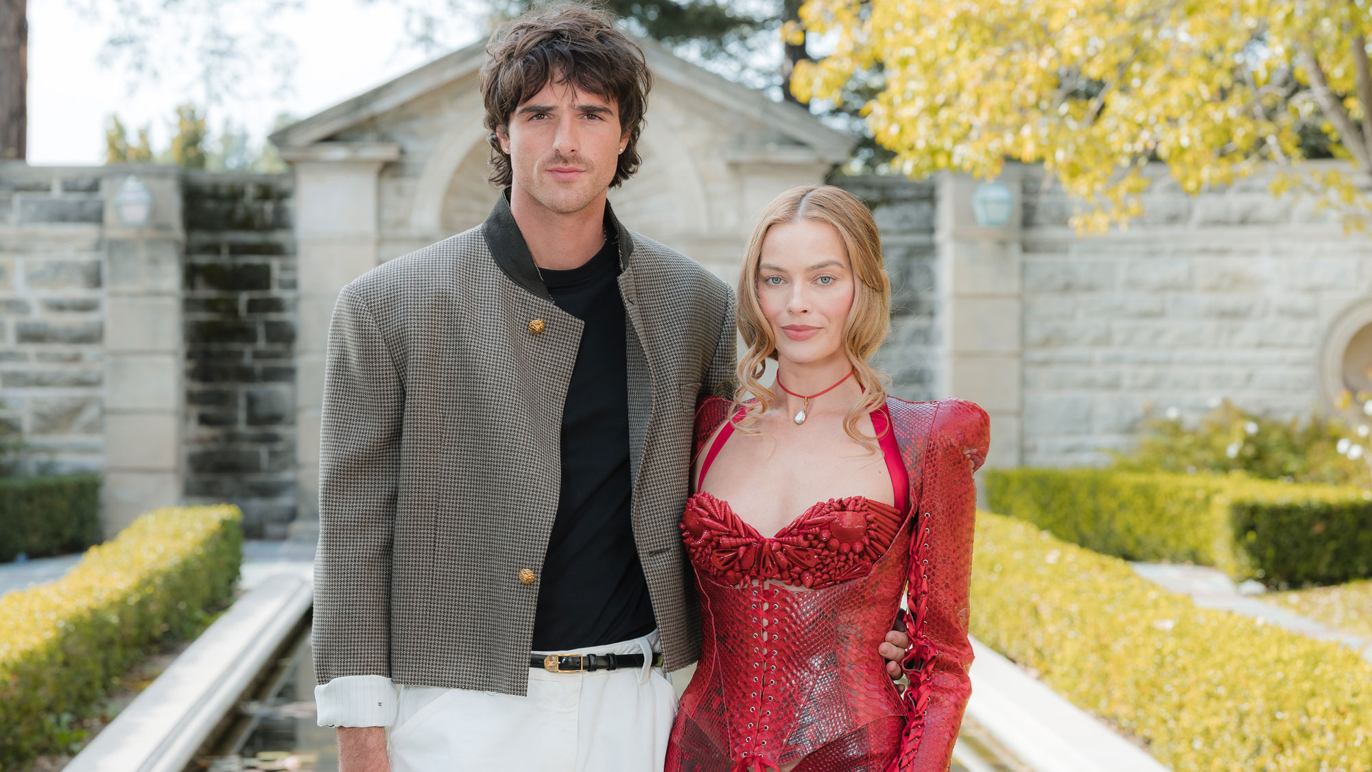 Margot Robbie wears a red minidress posing with Jacob Elordi