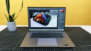 HP ZBook Studio 16 G11 mobile workstation on a white desk with a black table mat, against a yellow backdrop.