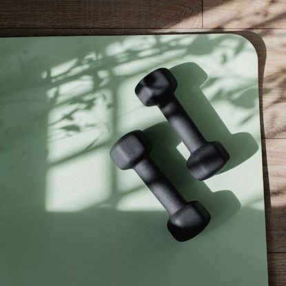 Two dumbbells on a green workout mat for use during a ten-minute Pilates workout