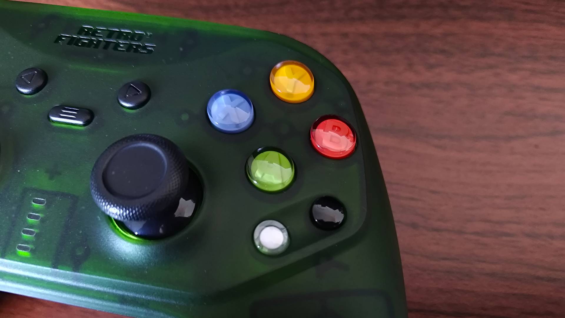 Close up of Retro Fighters Hunter face buttons on woodgrain desk.