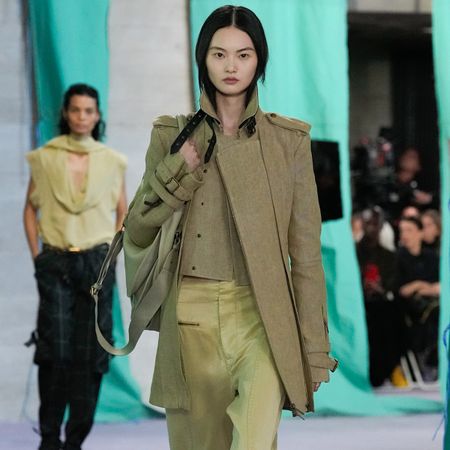 A model at the Burberry S/S 25 show wears a beige utilitarian jacket and gold satin pants.