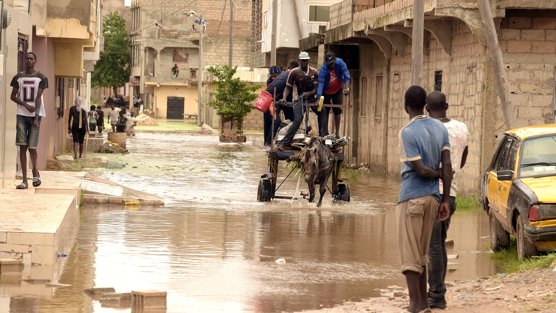 A man pulls a horse-drawn cart down a flooded street in a village.