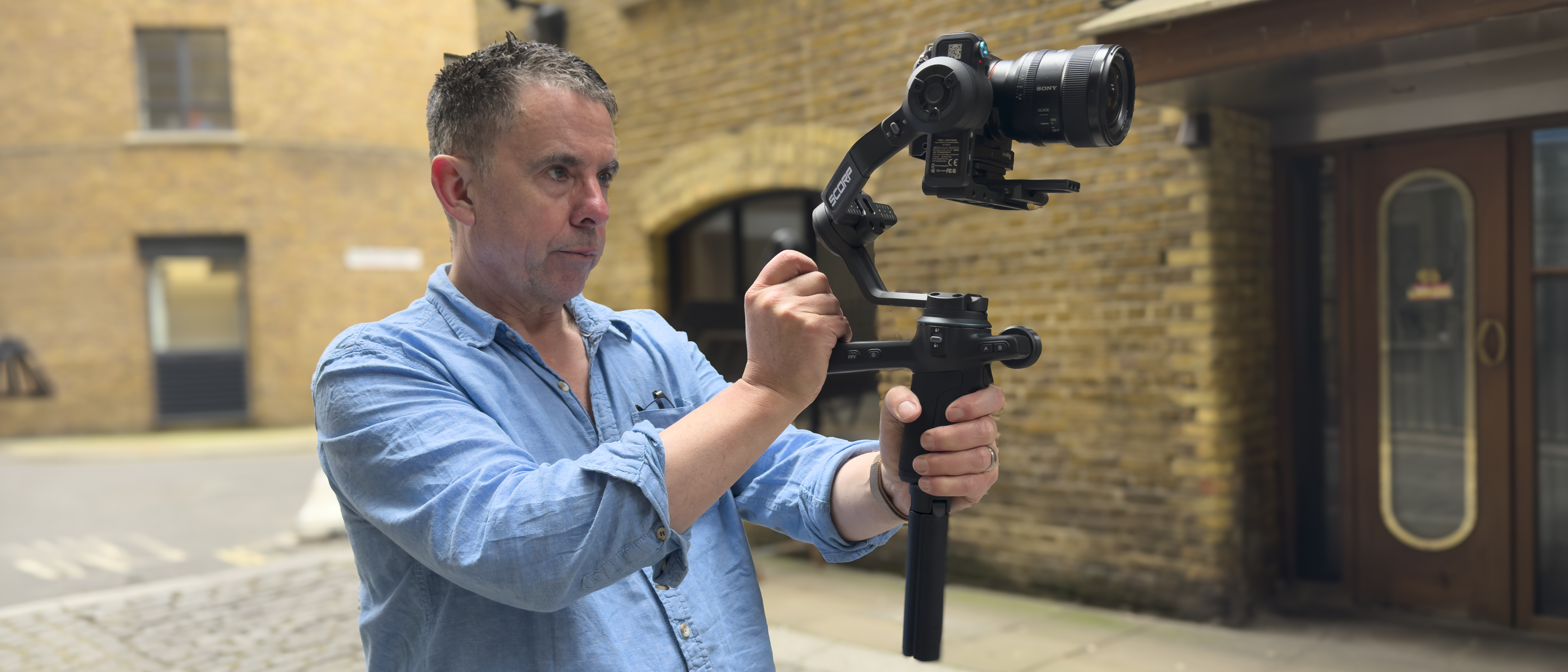 Man holding a camera mounted on a handheld gimbal in a cobbled street