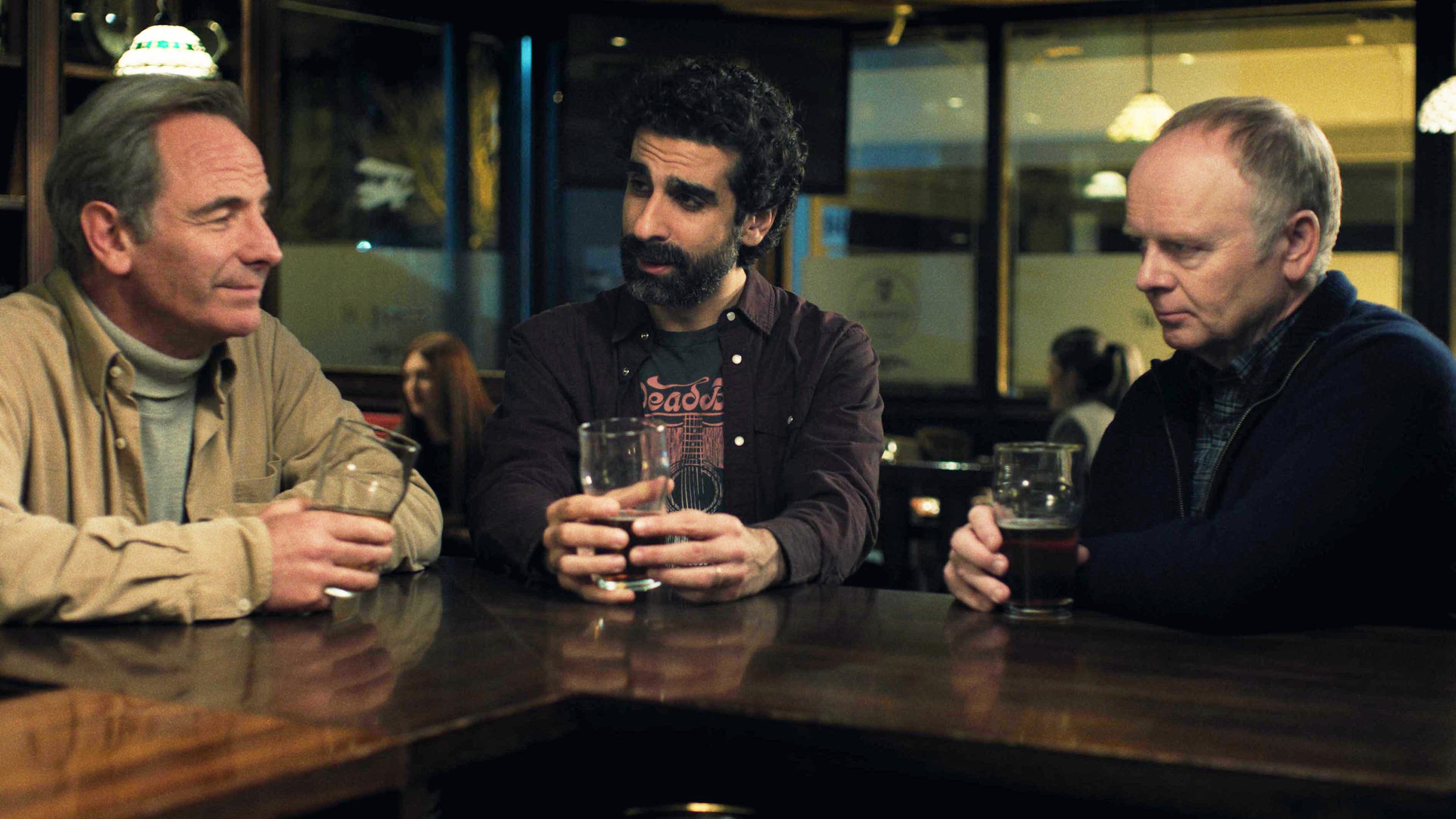 Huw and Patrick in the pub, sitting at the bar drinking pints of beer,