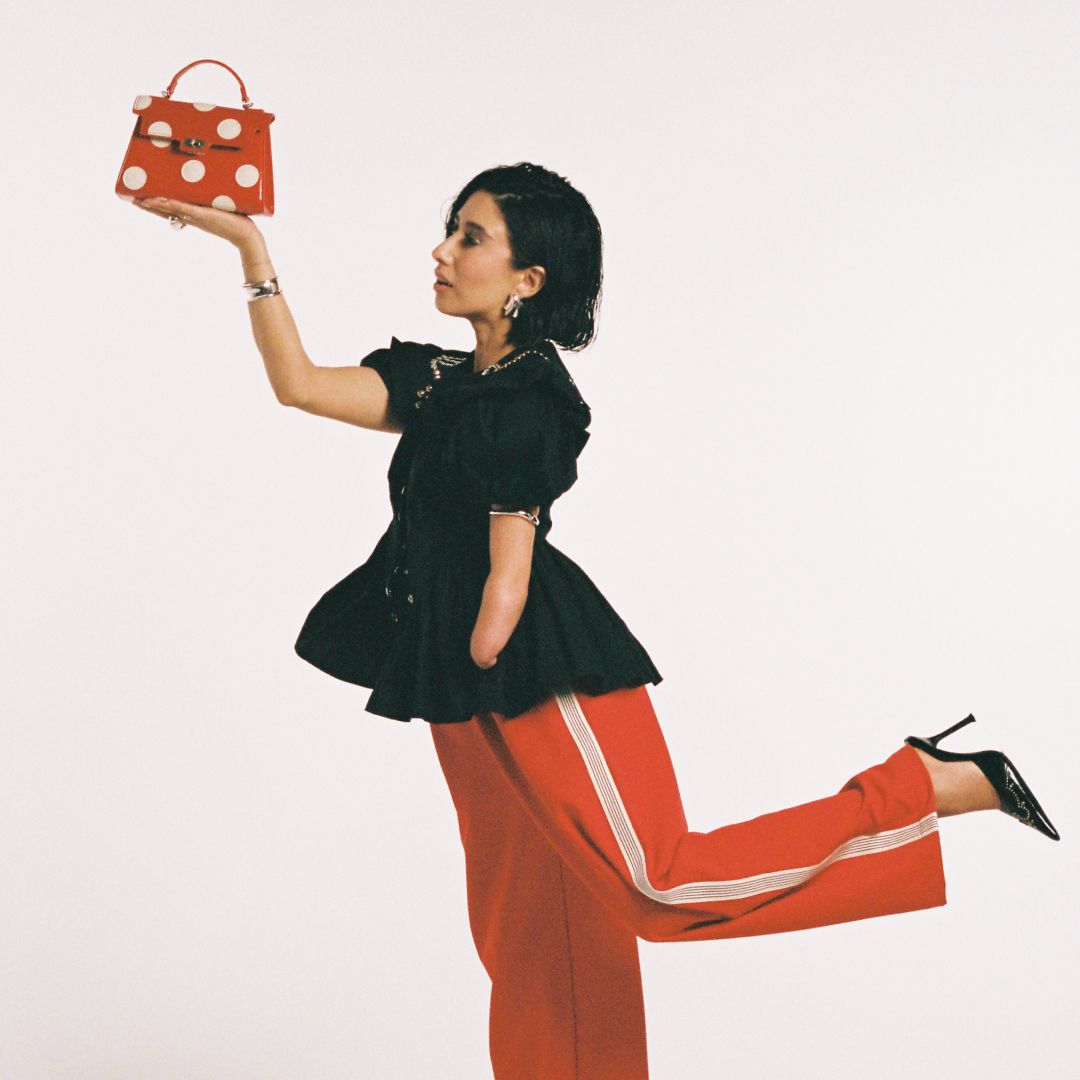 April Lockhart in red pants, a black shirt, a red and white polka dot bag