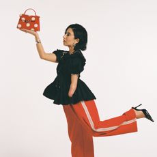April Lockhart in red pants, a black shirt, a red and white polka dot bag