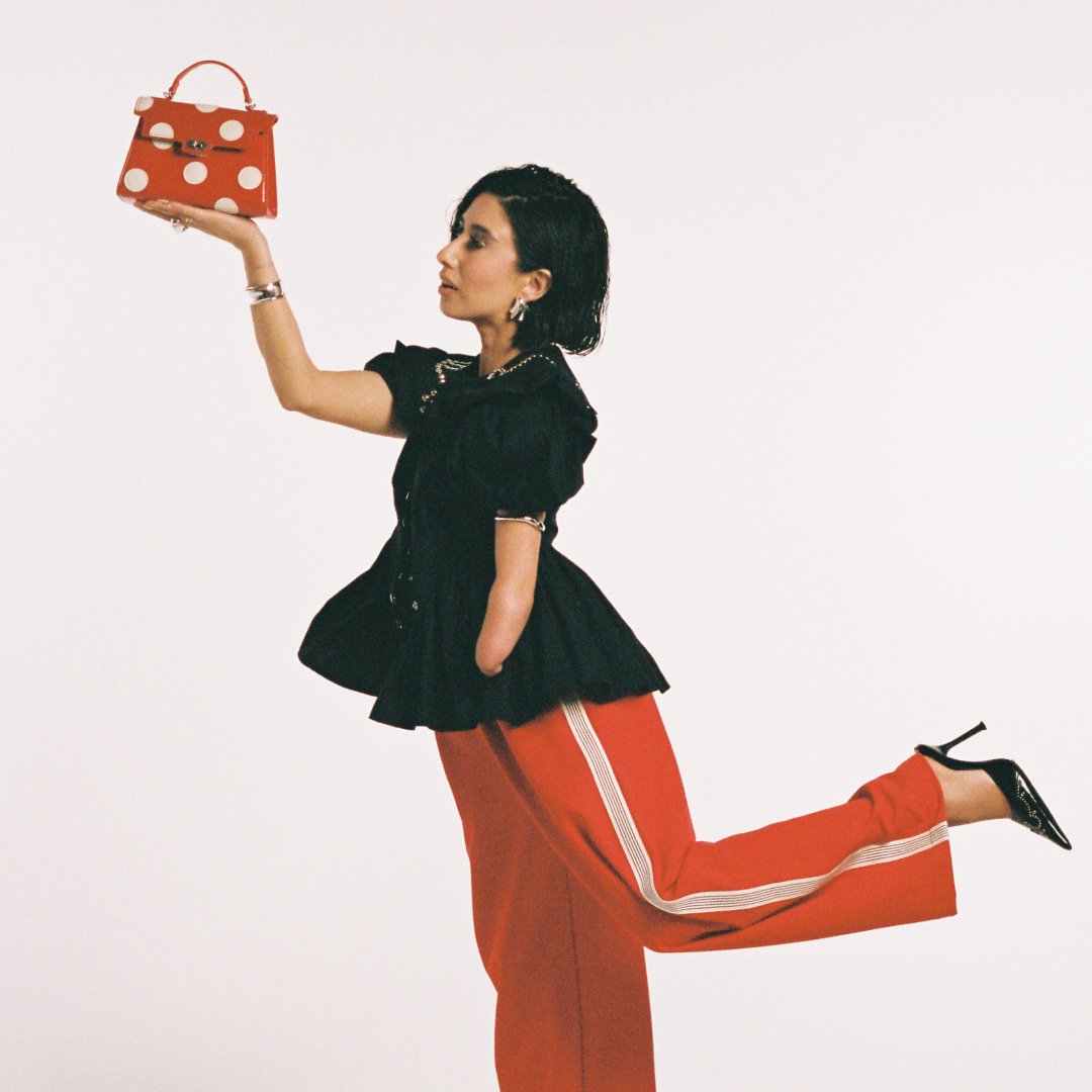 April Lockhart in red pants, a black shirt, a red and white polka dot bag
