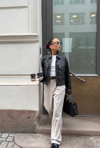 a photo of a woman's classic outfit idea with a leather jacket layered over a white t-shirt with tan trousers and black loafers