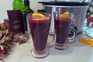 Mulled wine in two glasses with slow cooker, mulled wine sachets and brandy bottle in the background