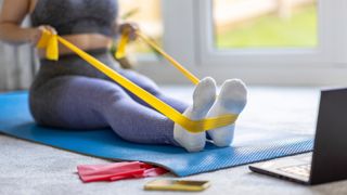 Mid adult woman practicing stretching exercise with resistance band at home