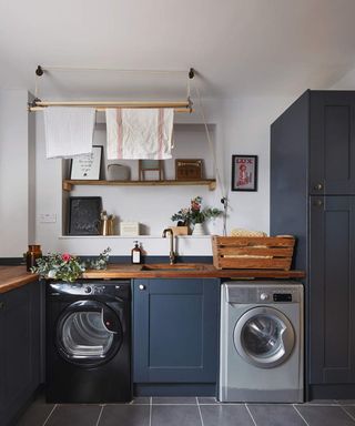 A laundry room with inky blue cupboards, washing machine and wooden shelves in alcove