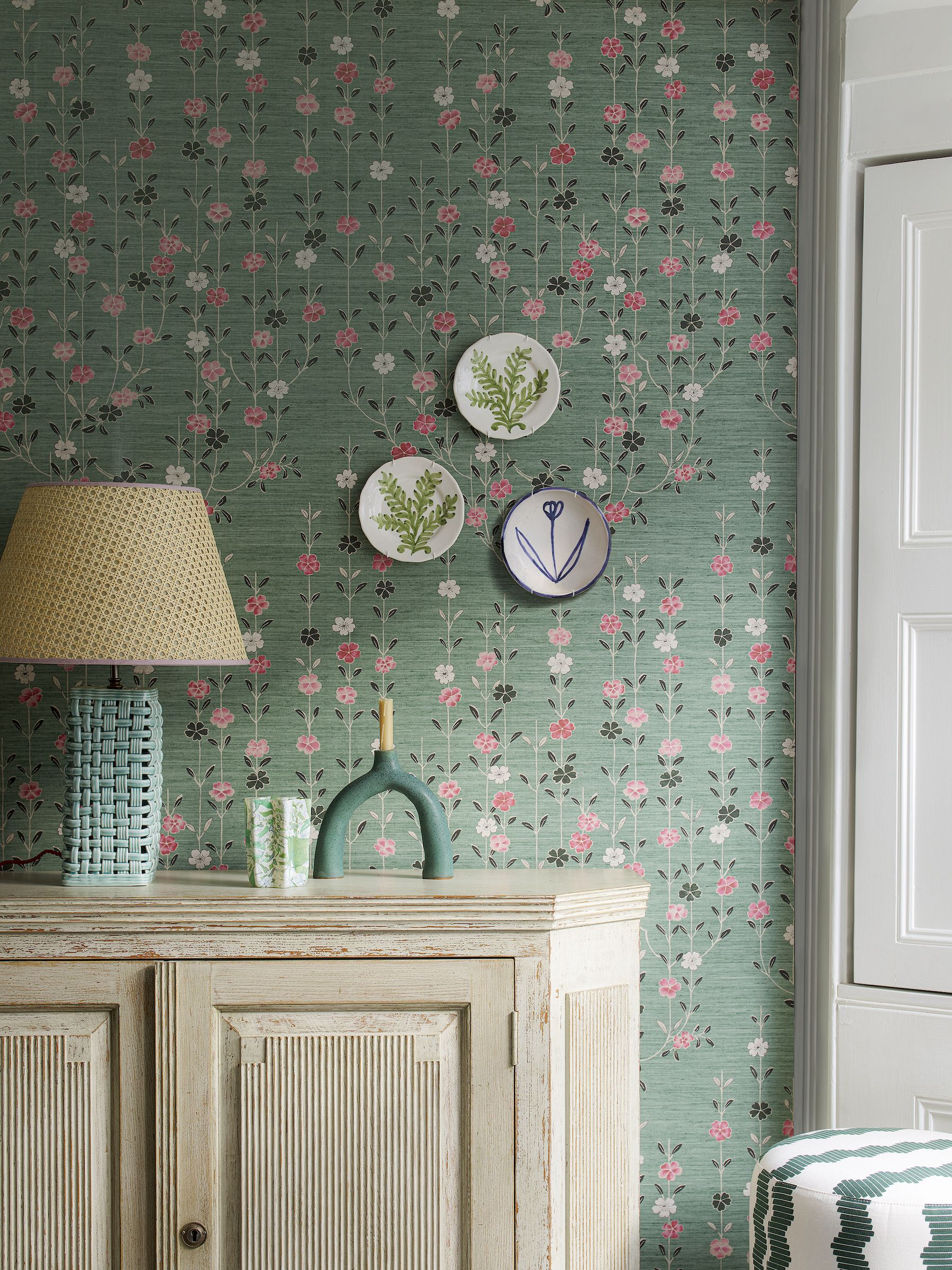 pink and green wallpaper behind console with plates on wall and lamp