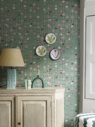 pink and green wallpaper behind console with plates on wall and lamp