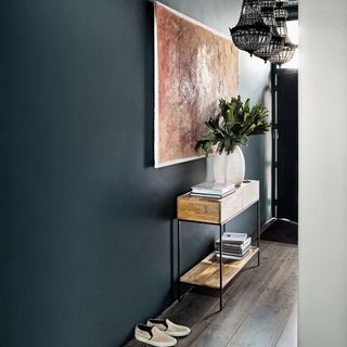 A dark grey hallway with wall art, a console table and three decorative ceiling lamps