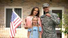 A soldier, with his wife and young daughter, holds a house key in front of a home with a U.S. flag in front.