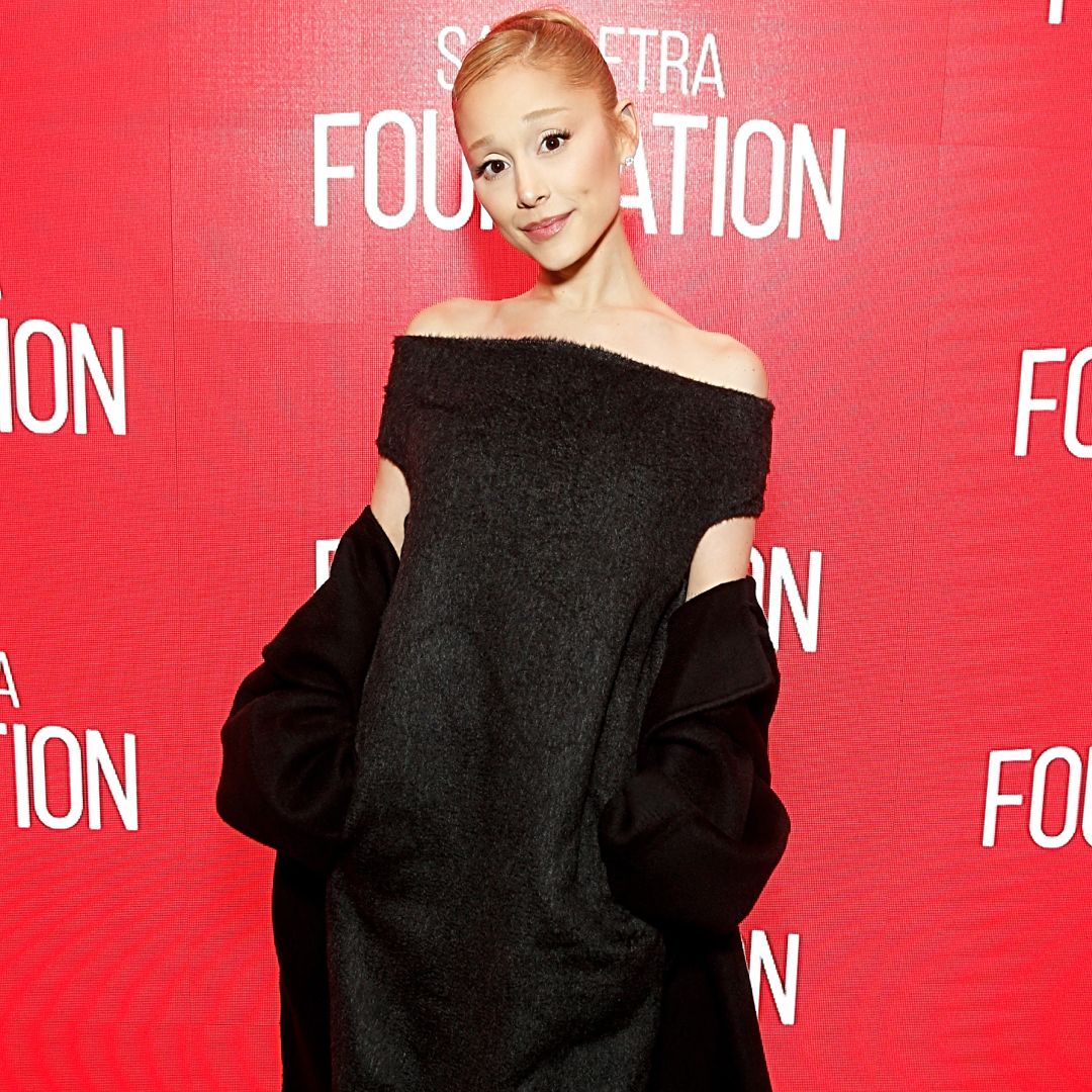 Ariana Grande wearing an off the shoulder black dress. She has her hair in a slicked back bun.