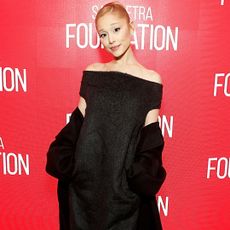 Ariana Grande wearing an off the shoulder black dress. She has her hair in a slicked back bun.