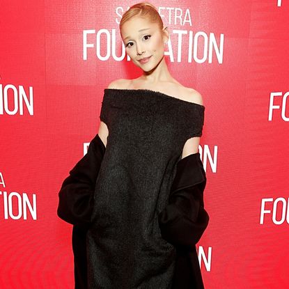 Ariana Grande wearing an off the shoulder black dress. She has her hair in a slicked back bun.