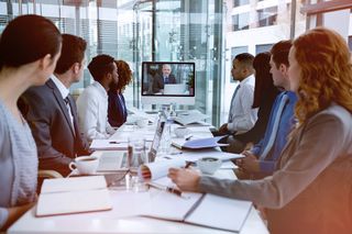 people sitting at a meeting room table watching video conference screen
