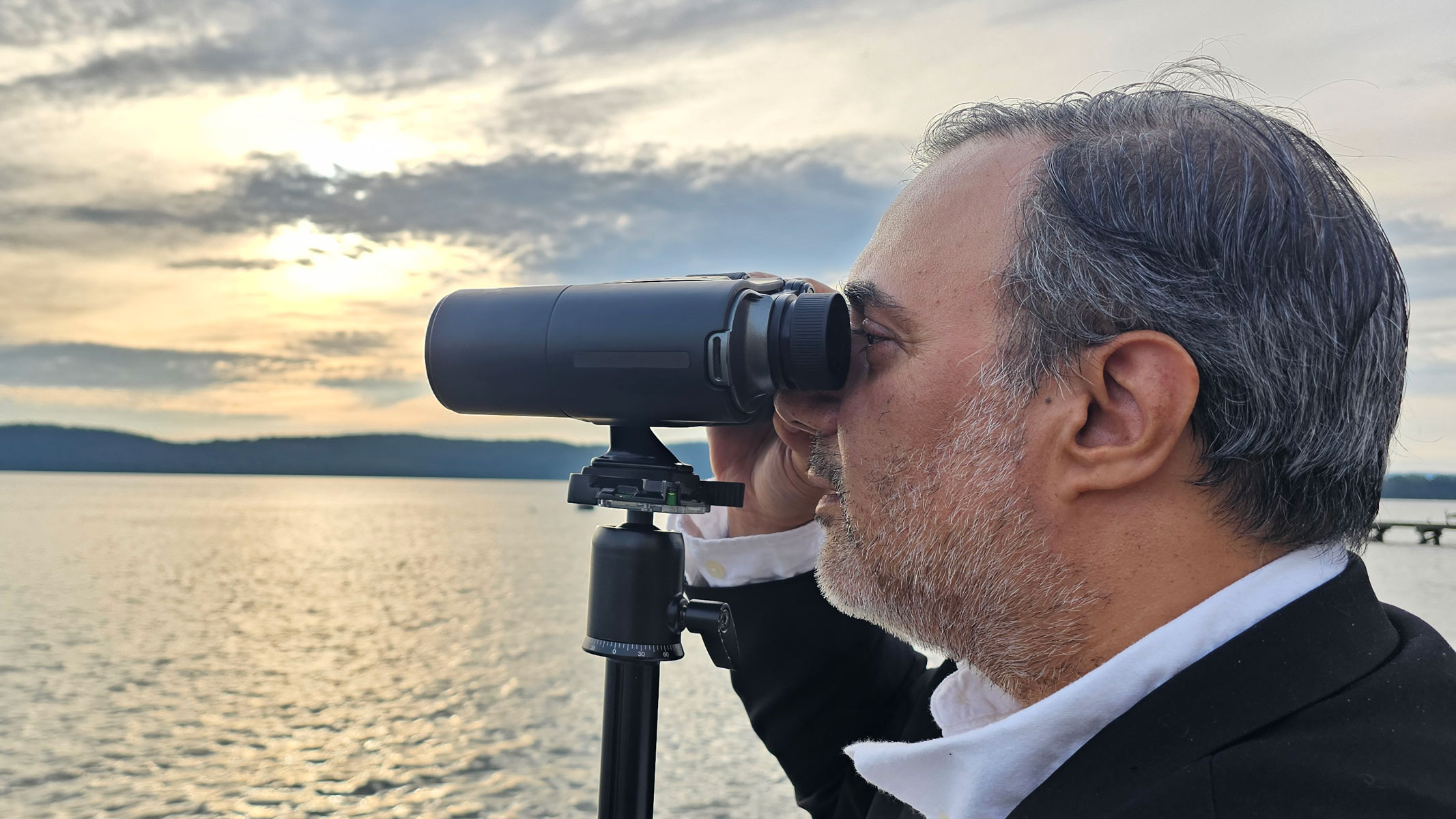 A man looking through the Unistellar Envision smart binoculars with a sunset in the background.