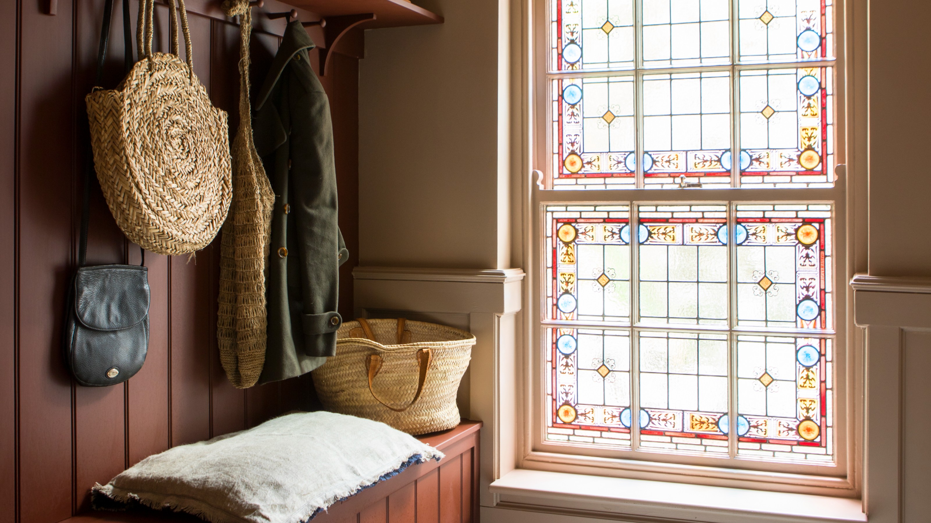 A hallway painted in light pink with a panelled wall in burgundy and a stained glass window