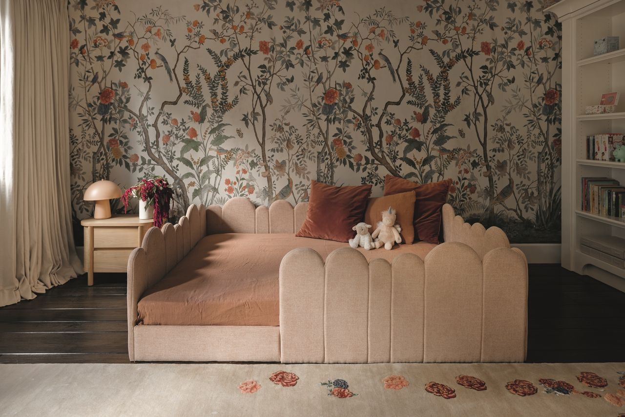 kids bedroom with scalloped pink bedframe, gucci wallpaper, built-in bookshelf, side table with mushroom lamp, dark timber floorboards, and white rug with patterns on it