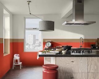 A kitchen with red and brown color blocked wall decor with island in centre of kitchen, red stool and grey ceiling pendant light