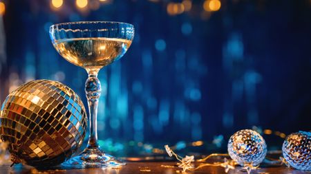 A glass of champagne and New Year's decor against a royal blue curtain background.