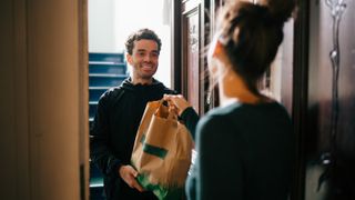 Smiling delivery man delivering bag to woman standing at doorway
