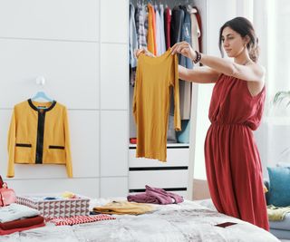 woman holding up yellow jumper stood next to wardrobe