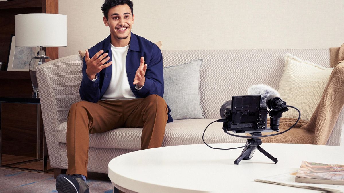 Man sitting on a sofa filming himself with one of the best lenses for vlogging