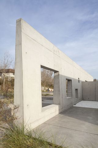 A concrete wall with openings of different sizes serves as a separator between the private area of the house and the street on the other side.