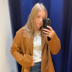 Woman wears camel coat, white T-shirt, blue jeans