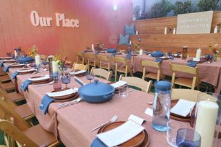 Two long dinner tables set with place settings and candles in front of a wood wall reading "Our Place" and a sign that says Archewell Foundation