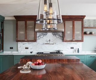 white and grey marble splashback with bookmatching effect in kitchen with a combination of dark wood and green cabinets