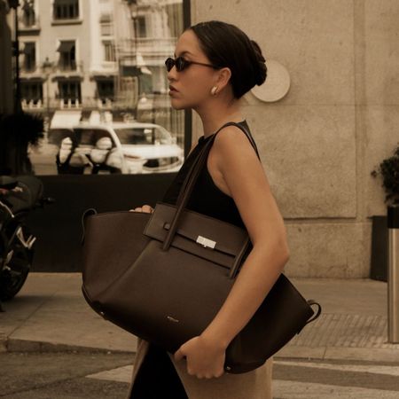 Woman wears leather jacket, carries DeMellier Brooklyn bag