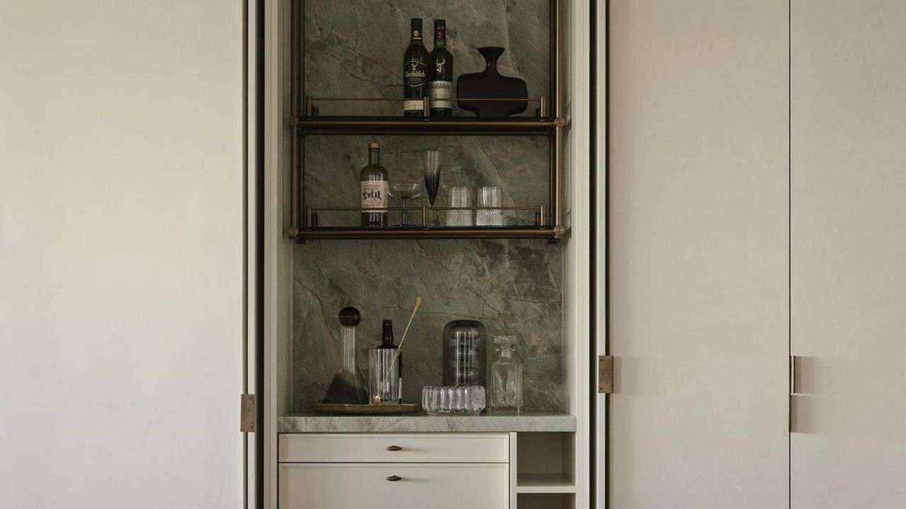 A home bar with a marble green backsplash and three shelving units as well as draws and a wine rack at the bottom. 